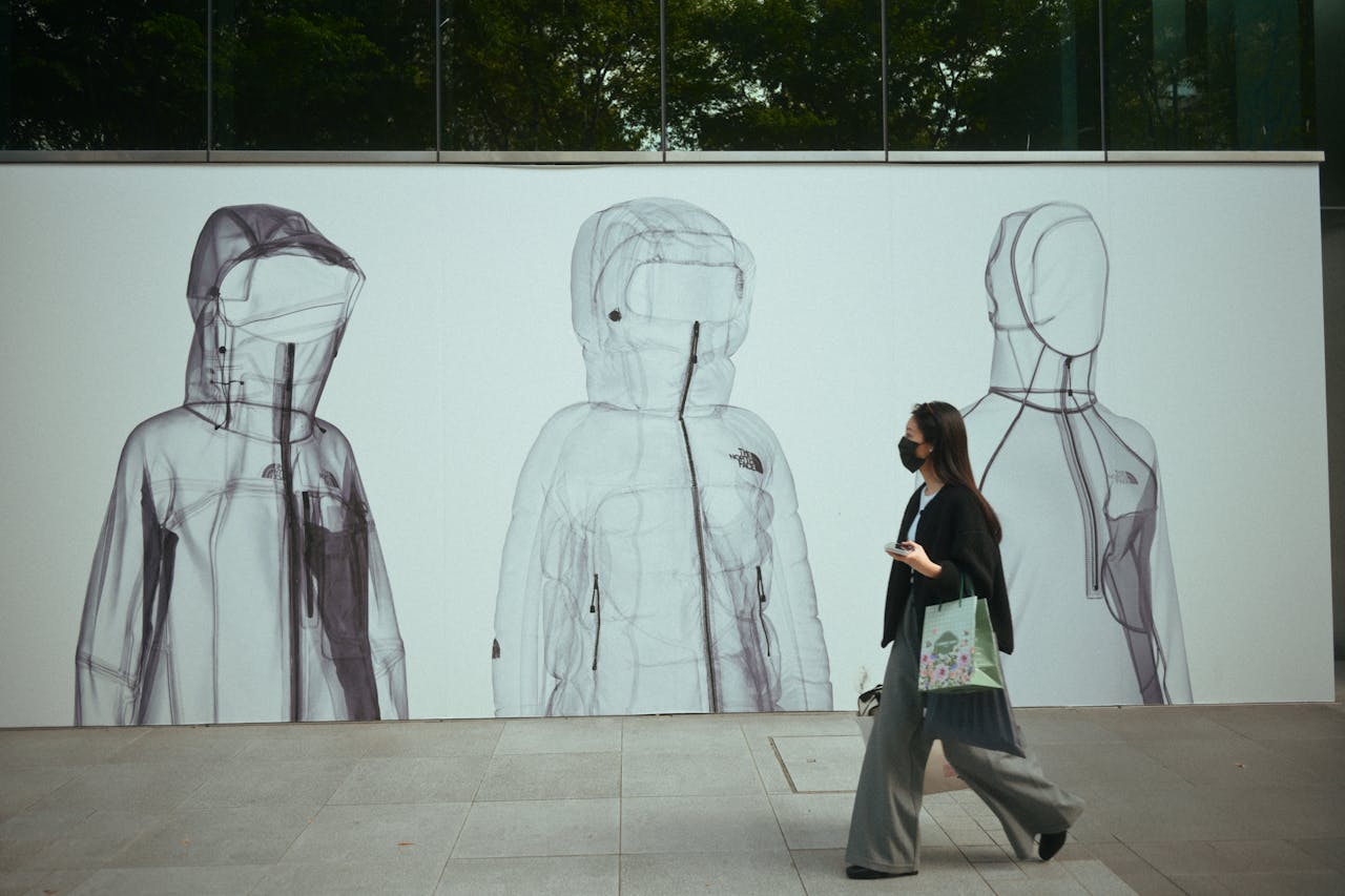 Masked woman walks by fashion art installation on modern street.